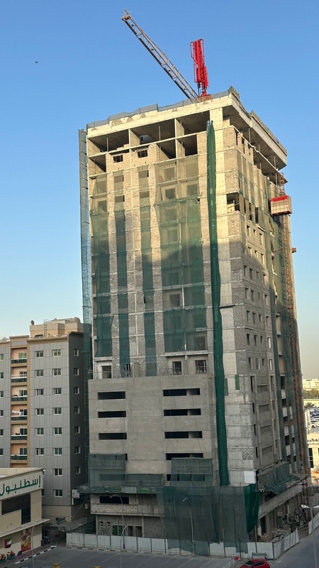 High-rise concrete structure under construction with a tower crane on top